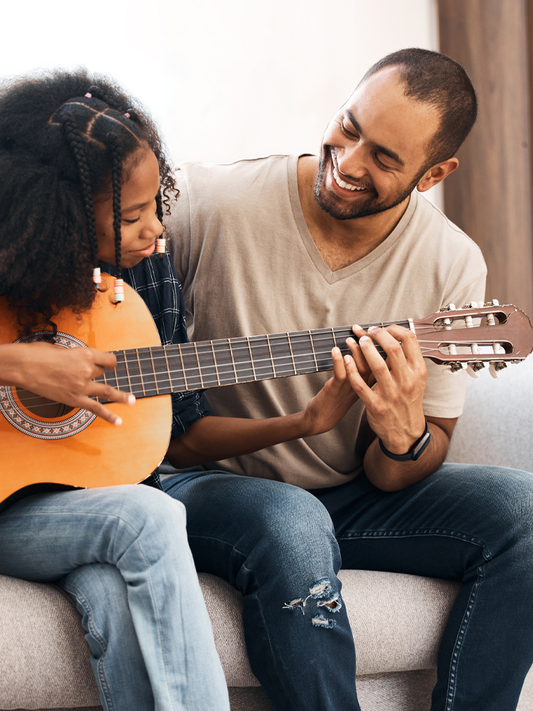 Image of father with daughter playing guitar.