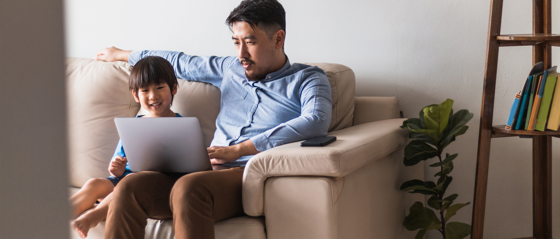 Image of father and son sitting on couch with laptop computer.