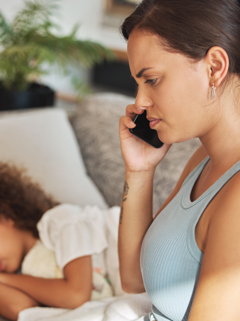 Mother on phone with child sleeping in background.