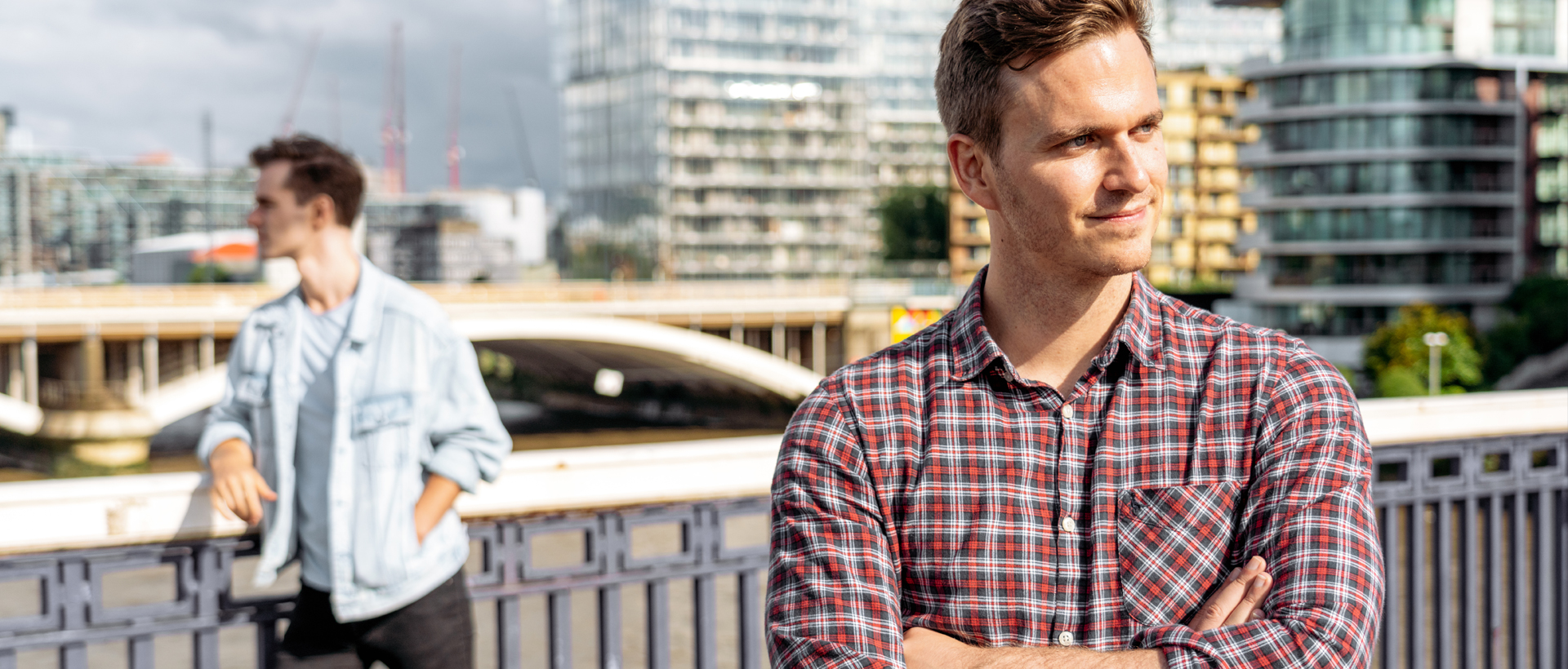 Image of two men standing on a bridge looking away from each other not speaking.