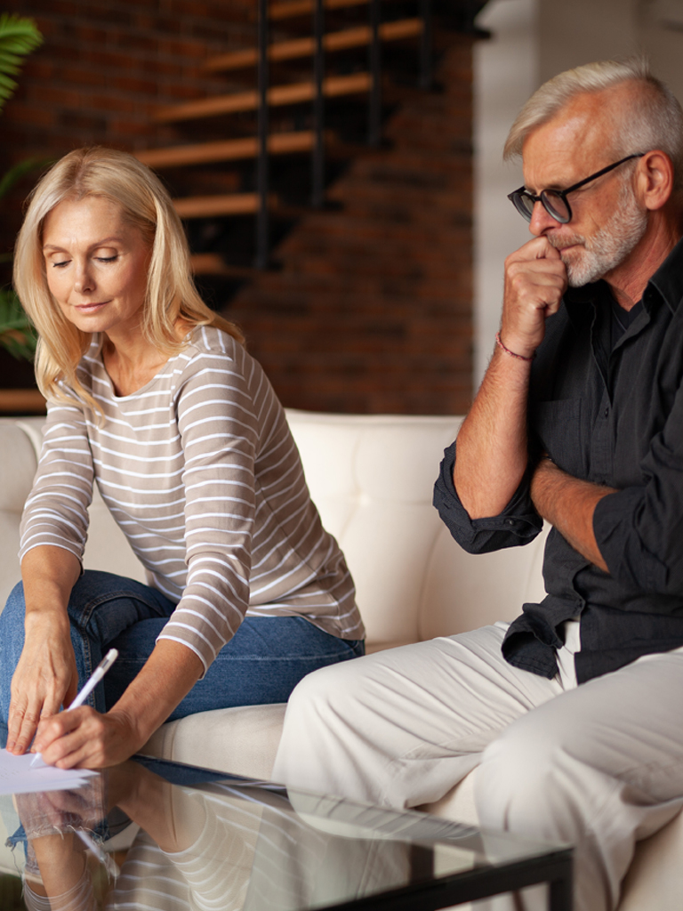 Man and woman sitting on couch signing divorce papers.