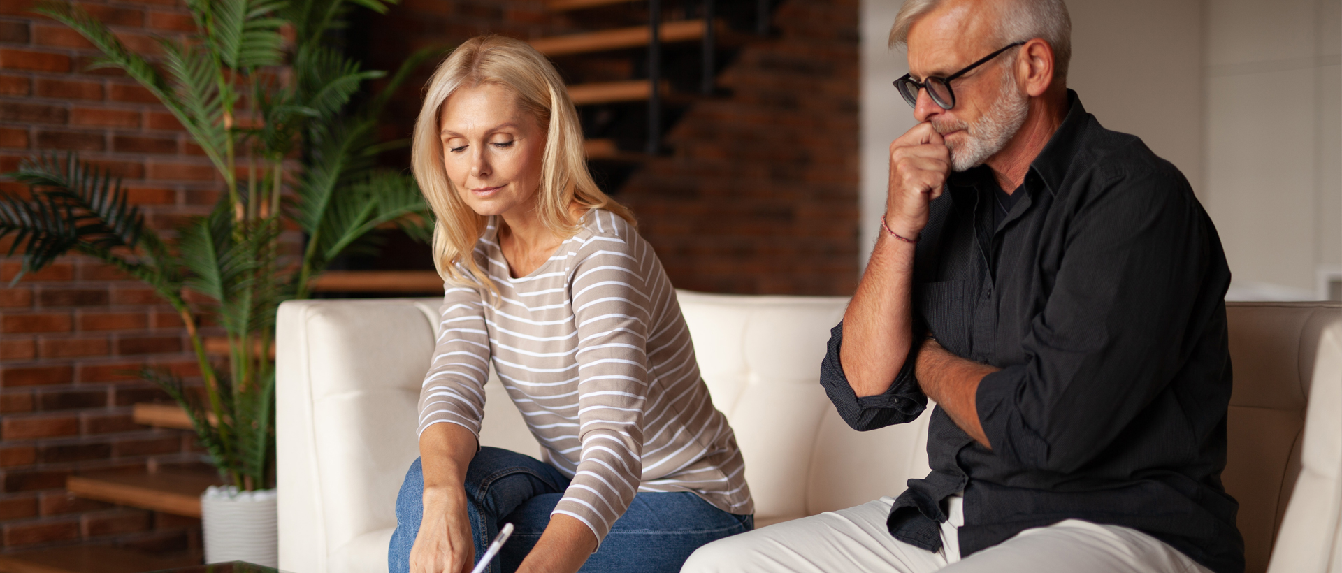 Man and woman sitting on couch signing divorce papers.