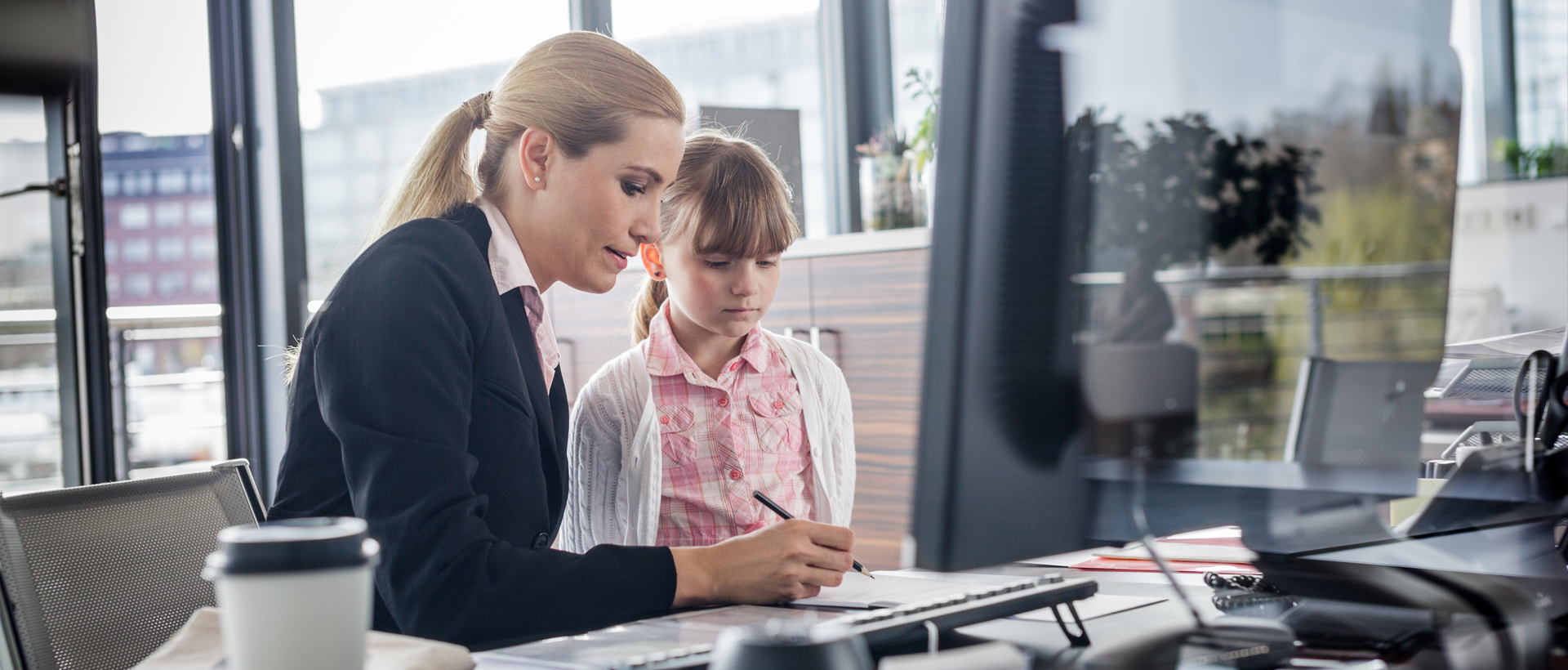 Woman working at desk with her daughter standing nearby.