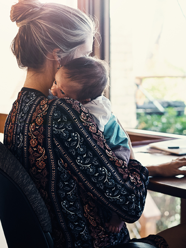 Woman working at desk holding baby.