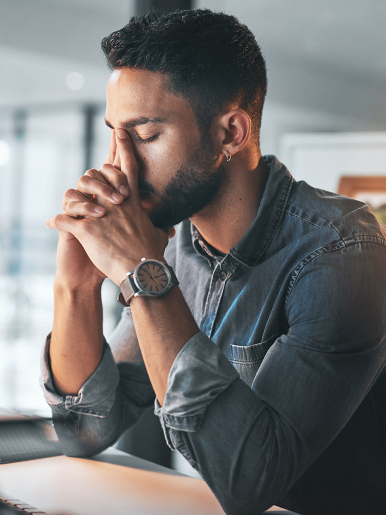 Concerned man sitting at desk with head in hands.