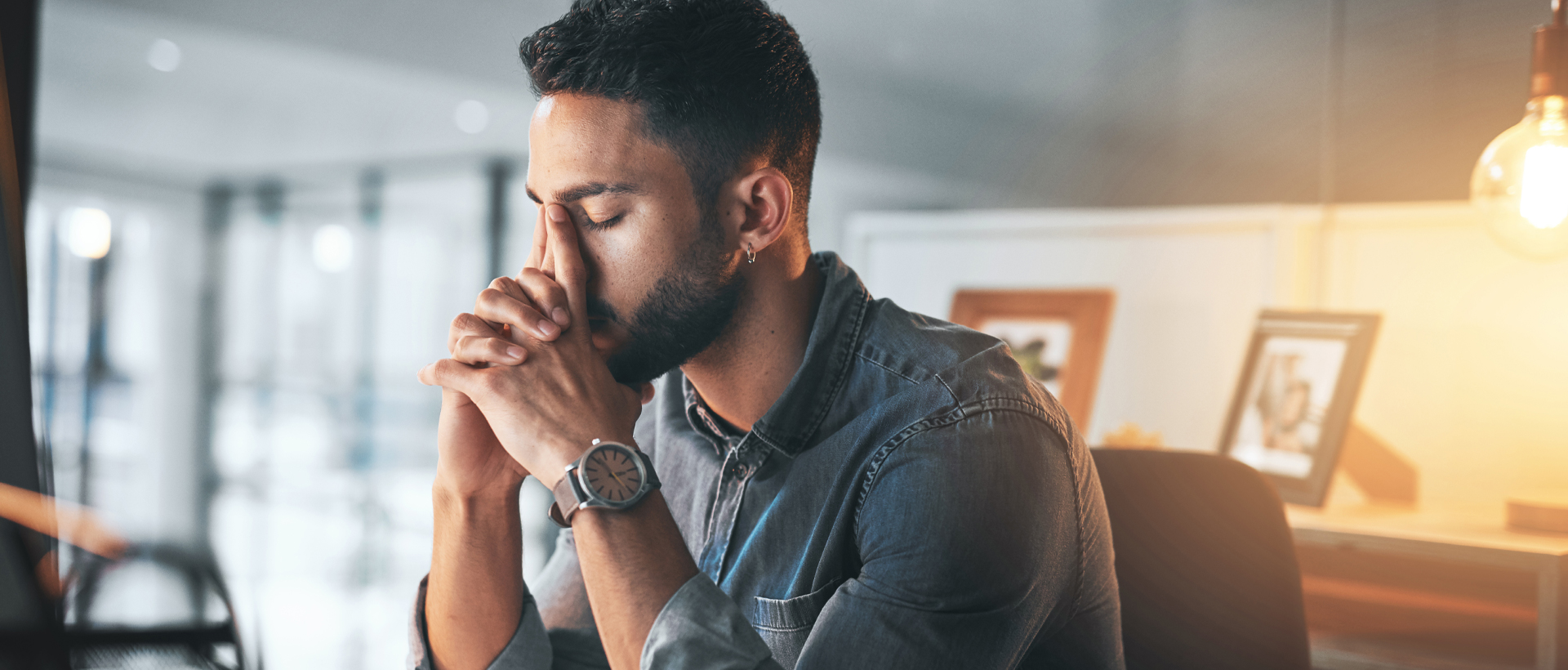 Concerned man sitting at desk with head in hands.